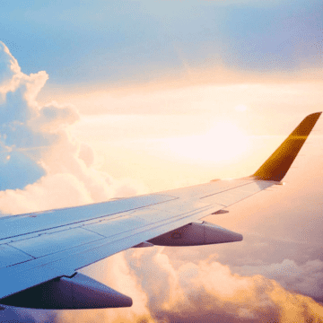 Blick aus dem Flugzeug über den Flügel in den sonnigen Wolkenhimmel: Freiheit.