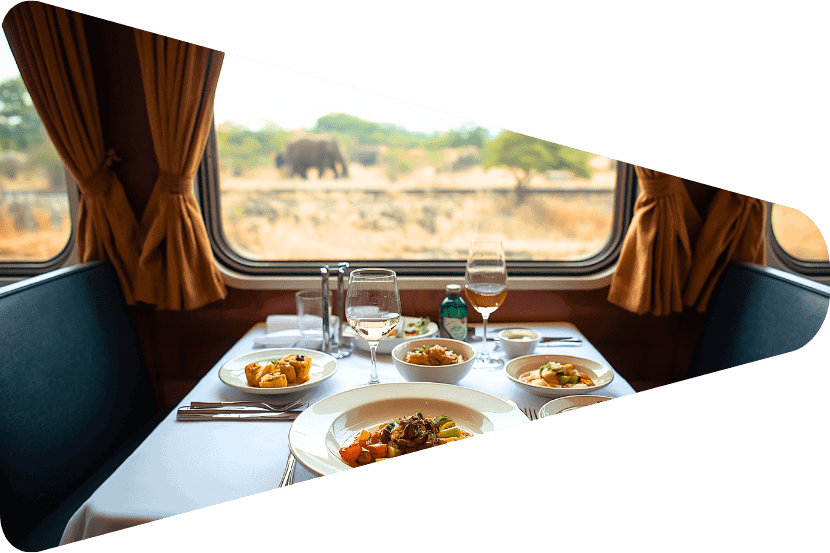 Gedeckter Tisch in einem Speisewagen eines Luxuszuges in Südafrika mit einem Elefanten vor dem Fenster. (Canva KI)