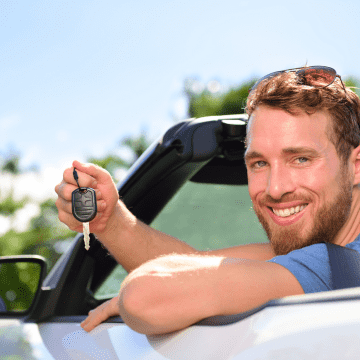 Der Mietwagenfahrer (Cabrio) zeigt lächelnd seinen Schlüssel.